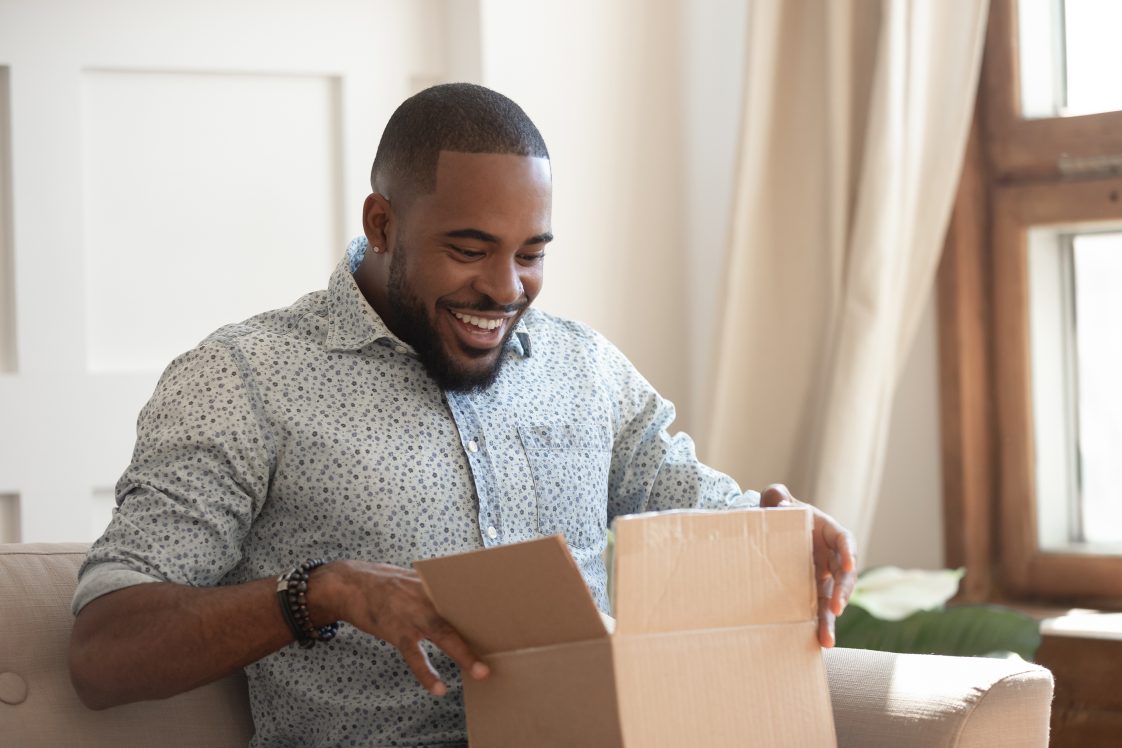 happy african american man unboxing a package at home