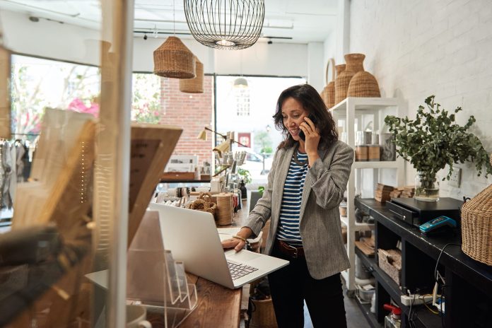 retailers in shop on phone using laptop