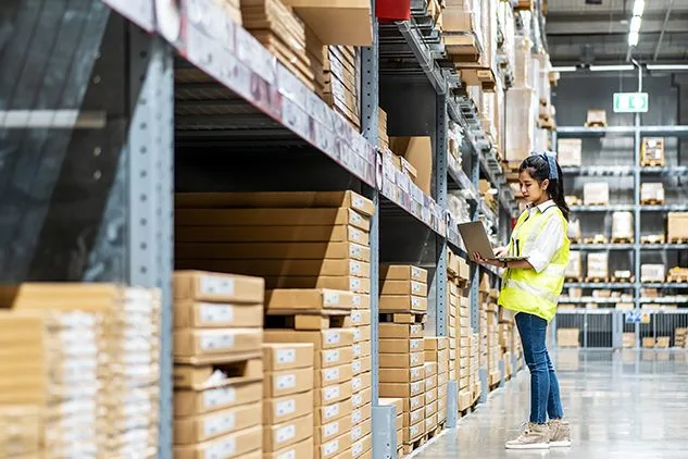 woman in warehouse looking at boxes on shelves with ipad