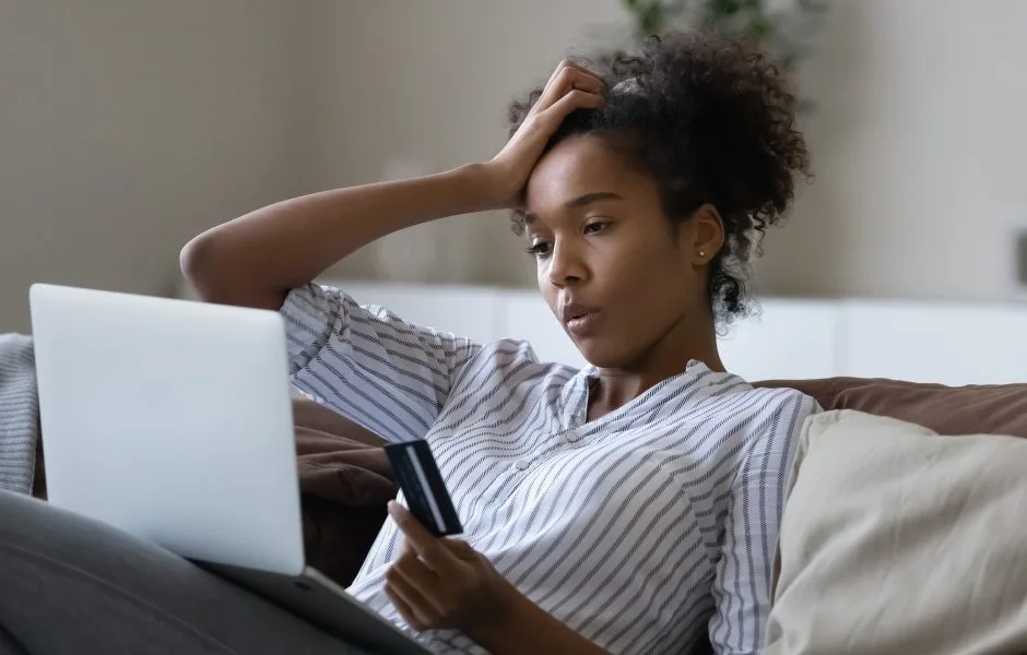 frustrated woman holding her credit card and looking at her laptop