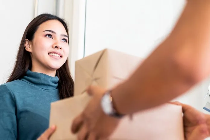 Delivery person hands parcel to woman in doorway.